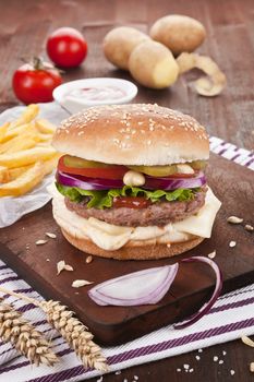 Country style hamburger on wooden board with potatoes, onions and chips.