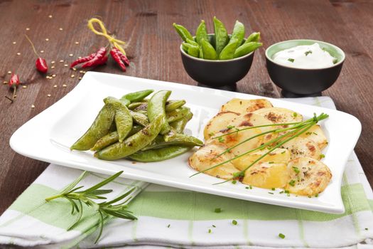 Baked potatoes with peas, herbs, chili pepper and sauce on wooden background. Delicious food.