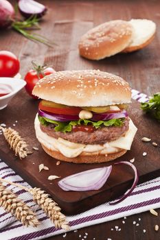 Fresh cheeseburger on wooden board decorated with fresh vegetables and wheat.