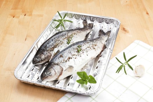 Two trouts with fresh herbs on grilling tray on wooden table ready for barbecue. Summer barbecue concept.