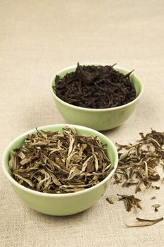 Green and black tea leaves in green bowls on brown natural background.