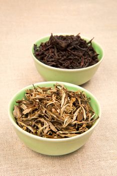 Green and black tea leaves in green bowls on brown natural background.