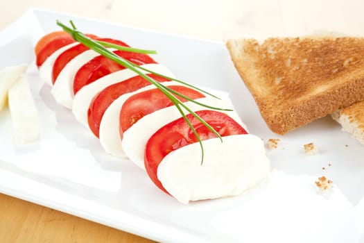 Mozzarella and tomato with toast bread on white plate decorated with fresh chive. 