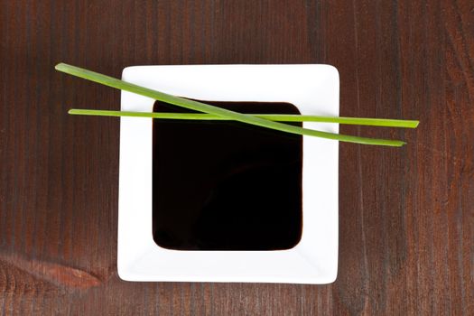 Soy sauce in white square bowl in dark wooden background with chive. Sushi concept.