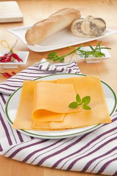 Cheddar slices on plate with herbs and pastry on wooden background. Cheese background. 