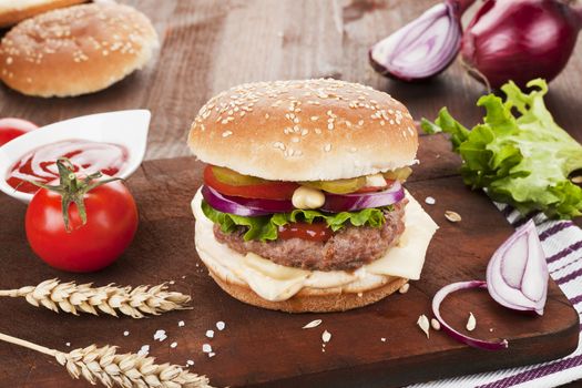 Big country style hamburger with tomatoes, onions on dark wooden cutting board. 