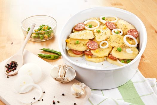 Fresh potatoes prepared for baking, pepper corns on wooden spoon and garlic on wooden table. 