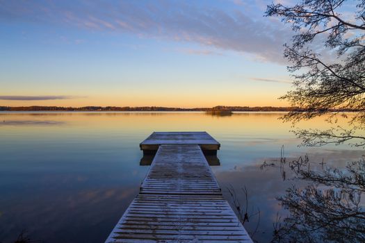 Scandinavian lake in the sunset with frozen  jetty and a tree silhouette