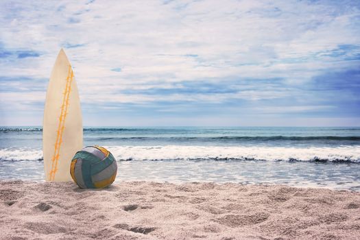 Surfboard and ball on empty beach against blue sky and turquoise ocean. Summer.