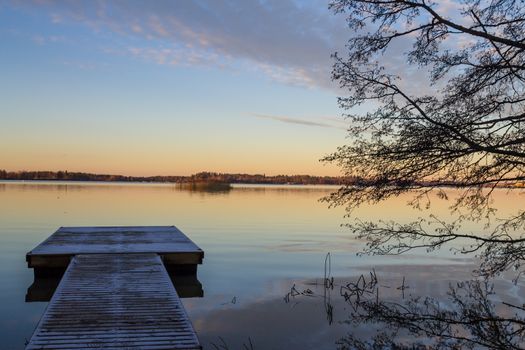 Scandinavian lake in the sunset with frozen  jetty and a tree silhouette