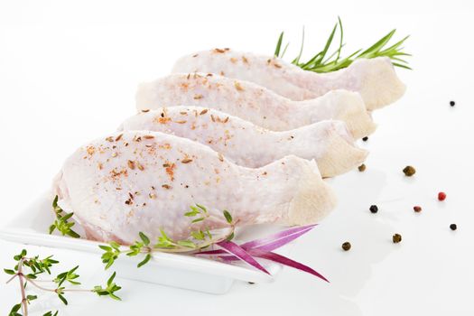 Chicken legs on white plate decorated with rosemary, onion and pepper corns. Poultry meat background.