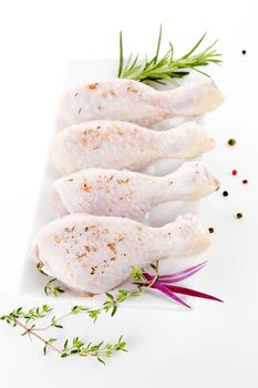 Four chicken legs on white plate with fresh herbs.