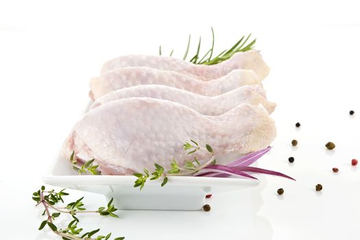 Four chicken legs on white plate decorated with fresh herbs on white background. 