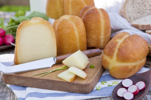 Traditional organic smoked cheese pieces on wooden board with fresh vegetables on organic farm.