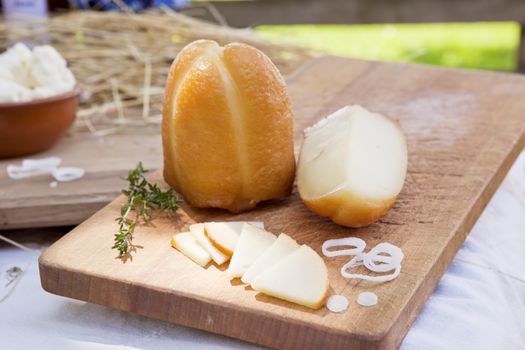 Smoked cheese piece and slices with herbs and onions on old wooden board on organic farm.