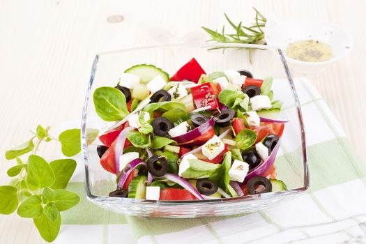 Fresh salad in glass bowl with fresh herbs. Olive oil dressing in background. 