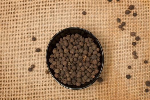 Peppercorns in black bowl on brown background.