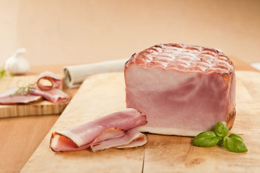 Ham piece and ham slices on wooden board with basil and garlic. Meat background.