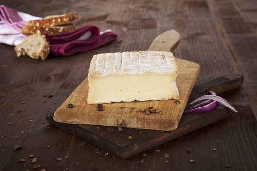 Cheese arranged on wooden board with bread, pepper corns and wheat. Agricultural vintage style concept.