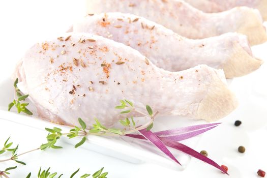 Raw chicken legs close up on white plate decorated with fresh herbs.