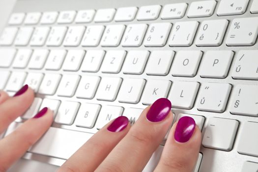 Female's hand with red nails touching a white metal keyboard.