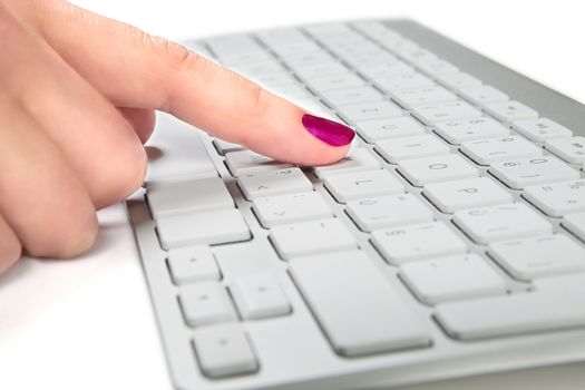 Female's hand with red nails touching a white metal keyboard.