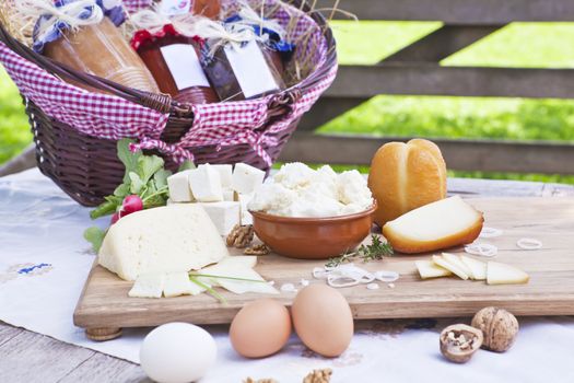 Traditional cheese variation on wooden board on organic farm. Basket with preserved marmalade in background.