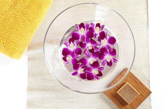 Wellness background, towel, soap and bowl with water and orchid flowers.