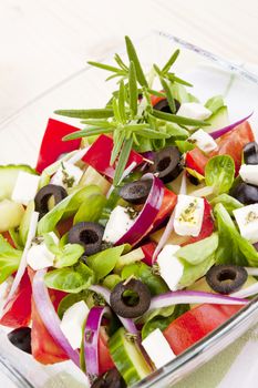 Fresh colorful greek salad with fresh herbs in glass bowl close up. 