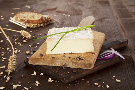 Cheese on wooden board with bread, onion piece, chive and wheat. Natural agricultural vintage style concept.