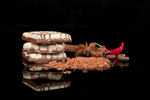 Delicious chocolate candy arranged on black background with cocao powder, cinnamon, coffee beans and chilli.