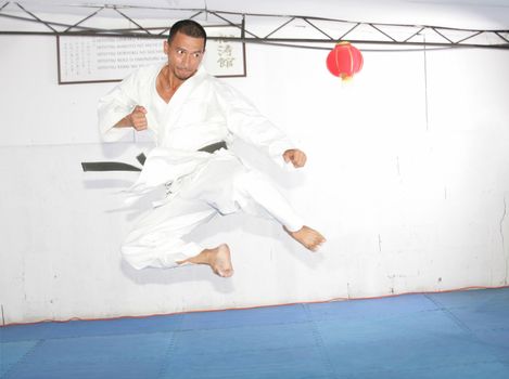 Black belt karate man jumping to give a high kick