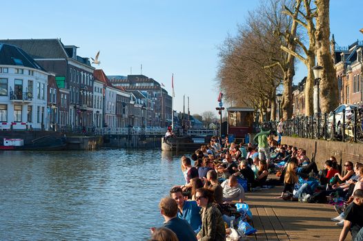 UTRECHT, NETHERLANDS - MARCH 09, 2014: People relaxing in the sun by a river canal in central Utrecht. Utrecht  is the capital and most populous city in the Dutch province of Utrecht