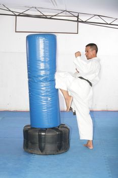 Athletic black belt karate giving a forceful knee kick during a training with a boxing bag