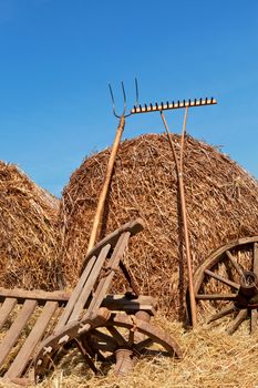 Traditional agriculture background. Hay bales, wooden wheel and wooden antique wheelbarrow against blue sky. 