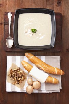 Mushroom cream soup with fresh pastry, fresh and dried mushroom on wooden background. Culinary healthy eating, rustic style.