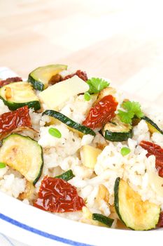 Delicious risotto close up with dry tomatoes, zucchini pieces and fresh herbs on white plate. Culinary vegetarian cooking.