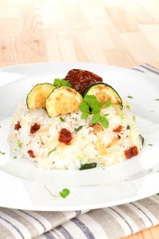 Luxurious risotto with dry tomatoes, zucchini pieces and fresh herbs on white plate. Culinary vegetarian cooking.