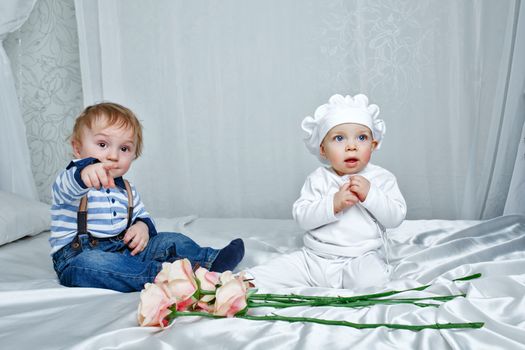 Cute brother and sister playing on a bed with silk sheets in the nursery