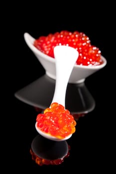 Luxurious red caviar on white spoon on black background with reflection. Culinary luxury foods.