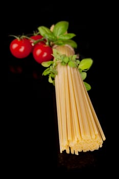 Raw uncooked spaghetti pasta, fresh tomatoes and herbs isolated on black background. Traditional italian pasta ingredients.