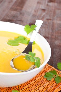 Delicious hot carrot soup with fresh herbs in white bowl. Healthy soup, rustic style.