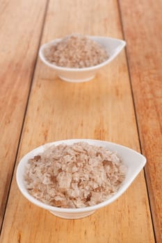 Sea salt flakes in white bowl on wooden background. Culinary cooking condiment.