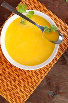 Delicious carrot cream soup in white bowl with spoon on wooden table. Culinary soup.