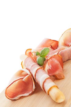 Breadstick grissini wrapped in prosciutto on wooden background. Culinary food background.