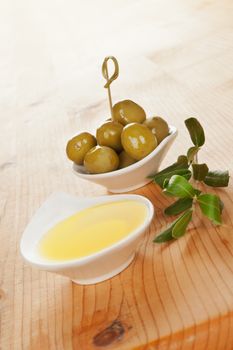 Olive oil and olives in bowls with twig on wooden background. Culinary traditional italian cooking.