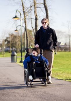 Father walking with disabled son in wheelchair at park