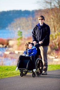 Father walking with disabled son in wheelchair at park