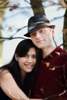 Young interracial couple hugging by lake, smiling together