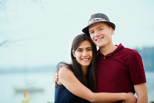 Young interracial couple hugging by lake, smiling together